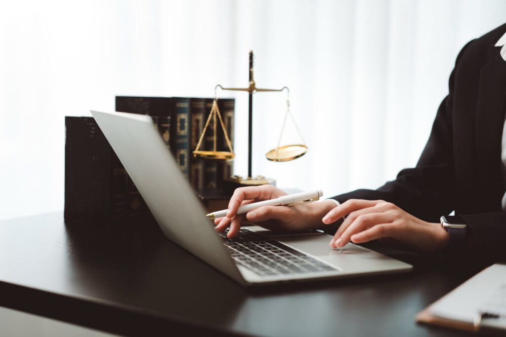 A person sitting at a desk holding a pen and typing on a laptop