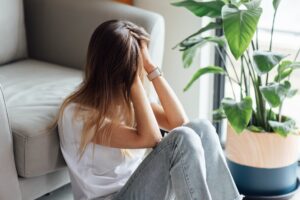 Unhappy young woman sitting on the floor against cough next to plant